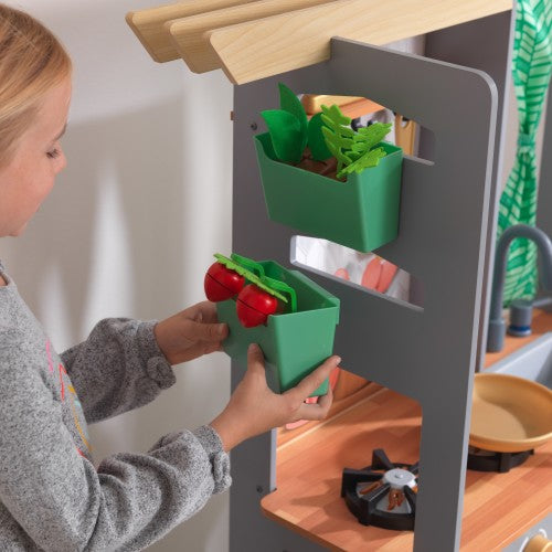 girl picking up vegetables fom kidkraft wooden kitchen playset