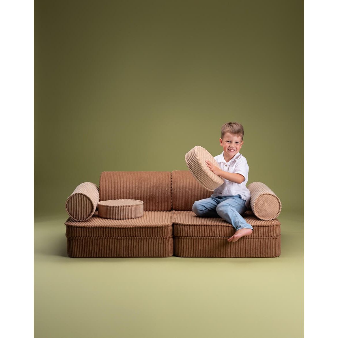 smiling boy sitting on Wigiwama Toffee Settee and holding cushion