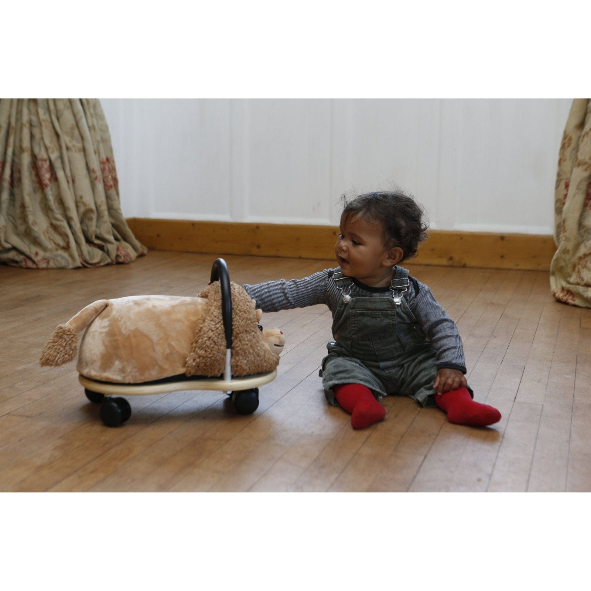 girl sitting on floor next to Wheelybug Plush Ride On - Lion