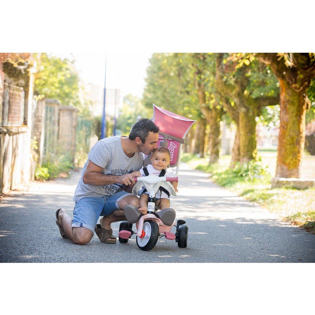 man kissing baby sitiing in pink Smoby Baby Balade Trike
