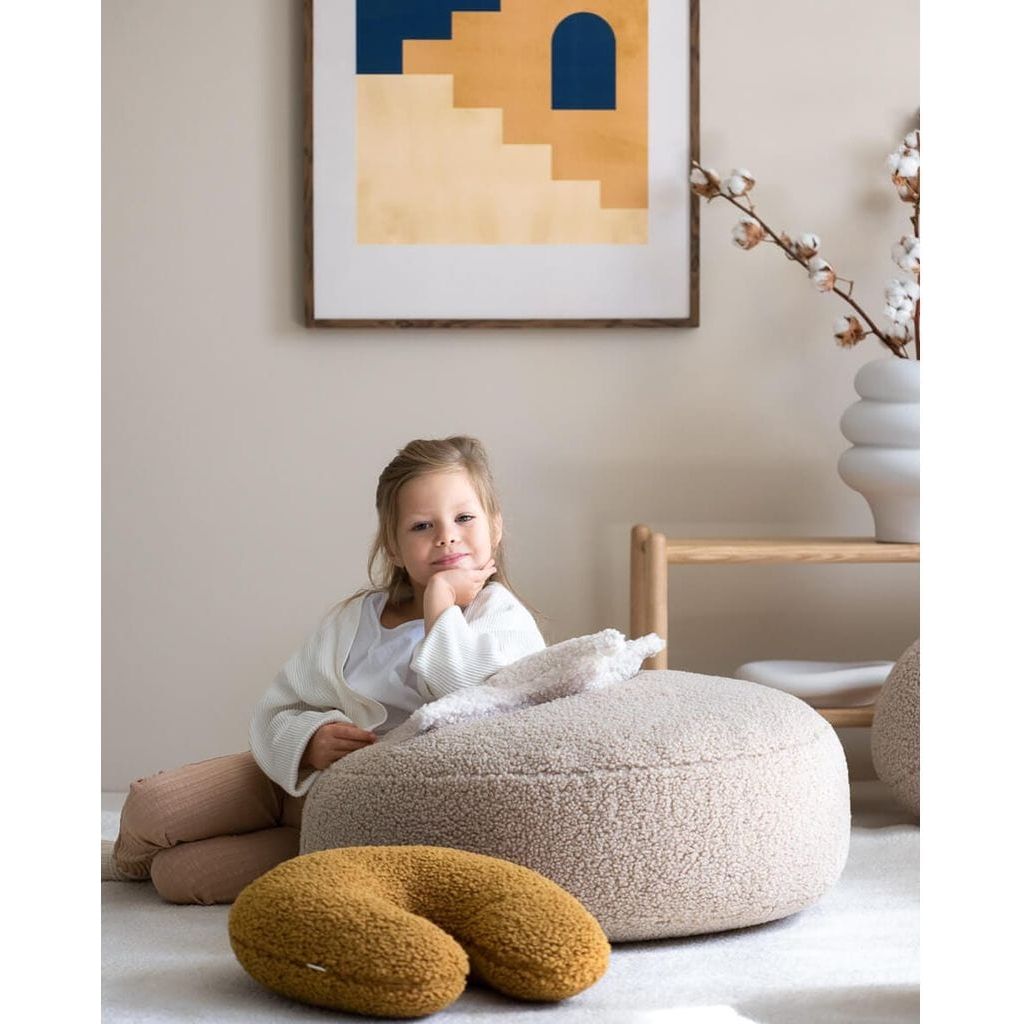 girl leaning on oatmeal ottoman next to Wigiwama Maple U Pillow