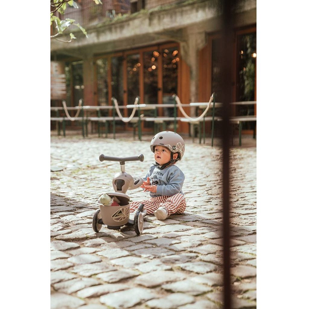 child sitting on cobbled street next to Scoot and Ride Highwaykick 1 Lifestyle Scooter- Brown Lines