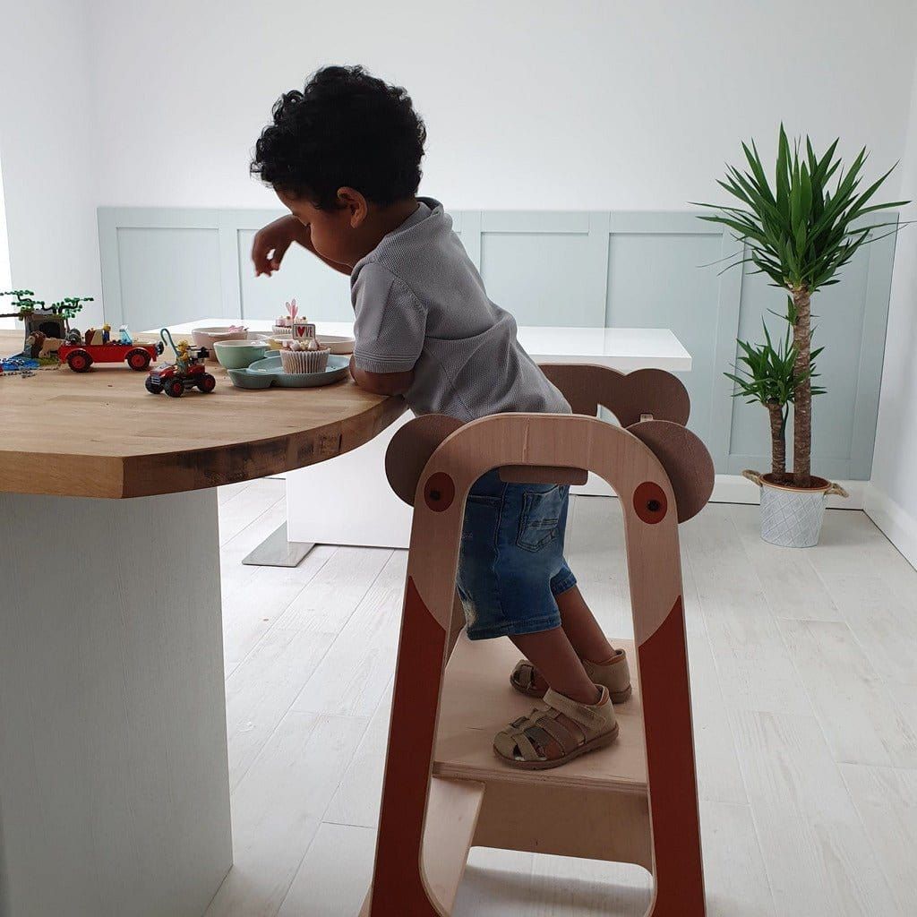 Little boy standing on Mama Toyz Kule Wooden Learning Tower making cakes
