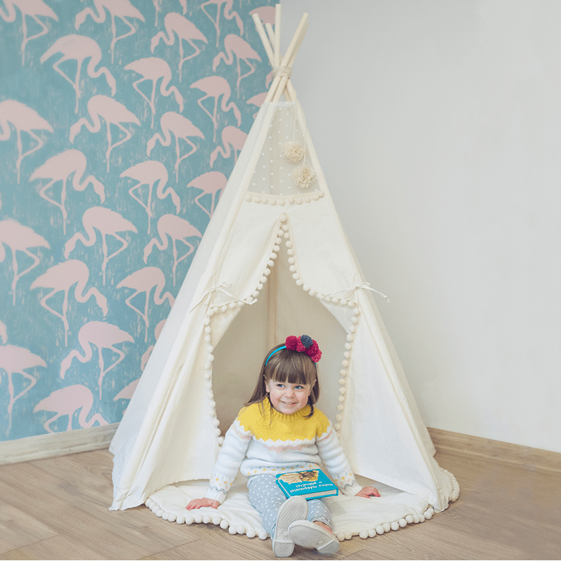 smiling girl sitting in MINICAMP Original Play Tent With Pompoms in playroom