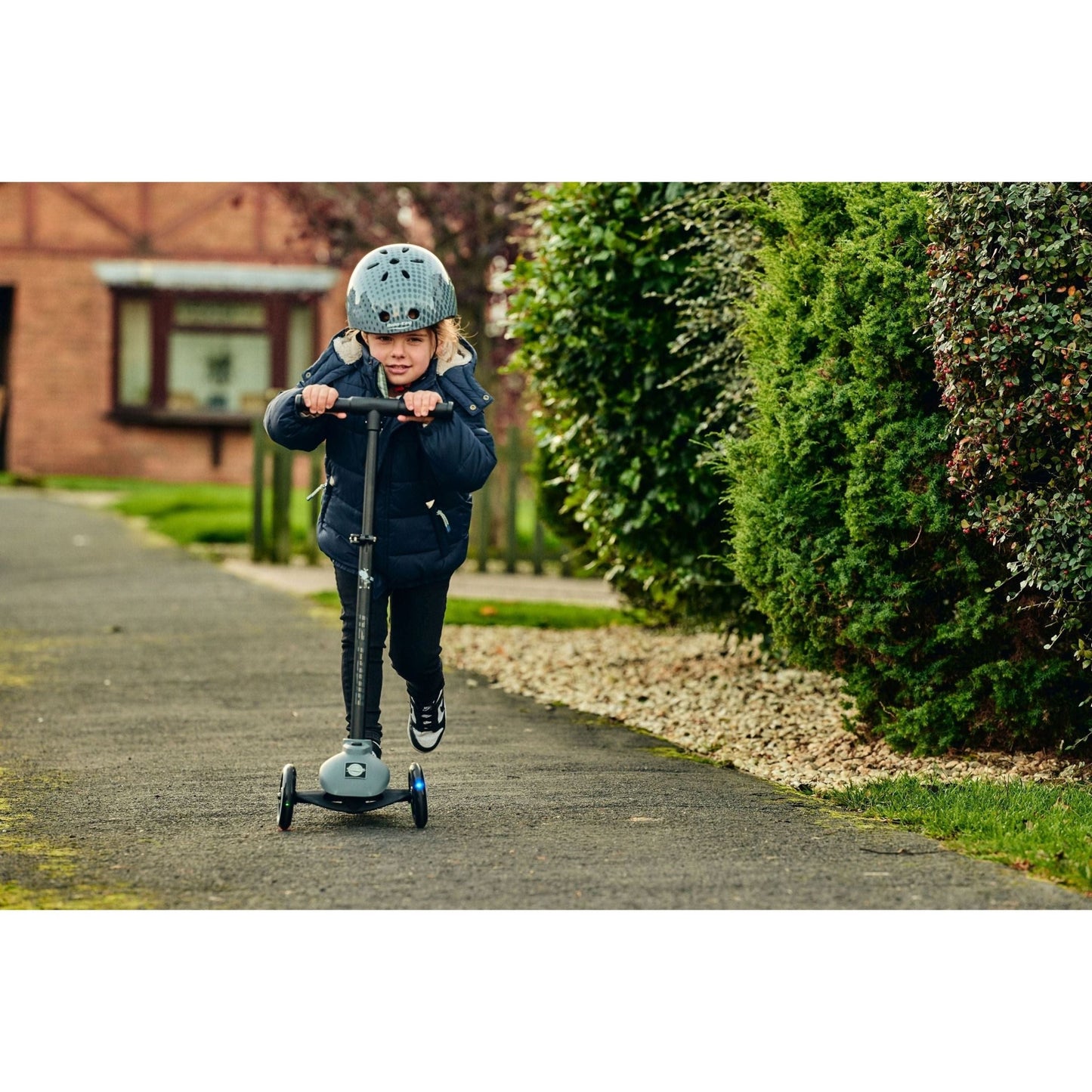 front view of girl riding ride-ezy scooter and wearing Ride-Ezy Hector 48-53cms Kids Helmet - Thunder Clouds