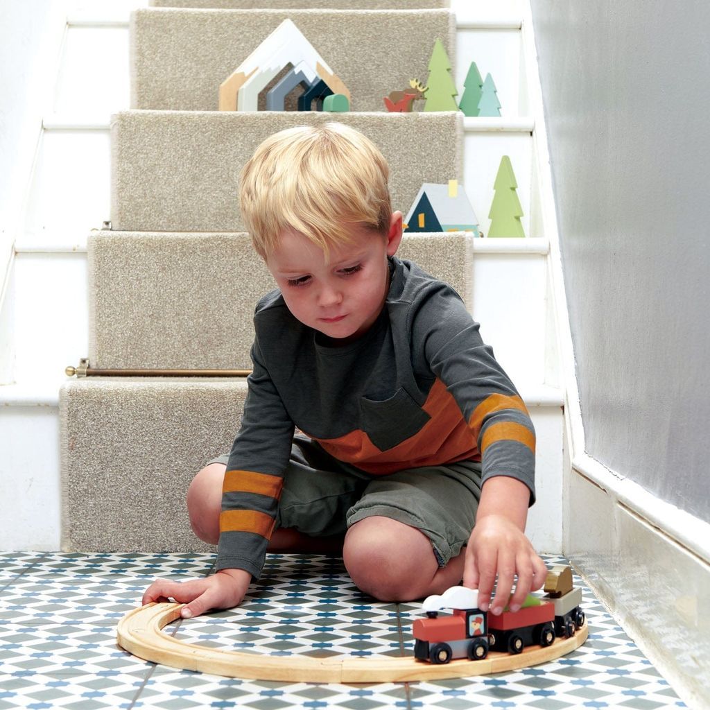 bot sitting at bottom of stairs playing with Tender Leaf Treetops Wooden Train Set