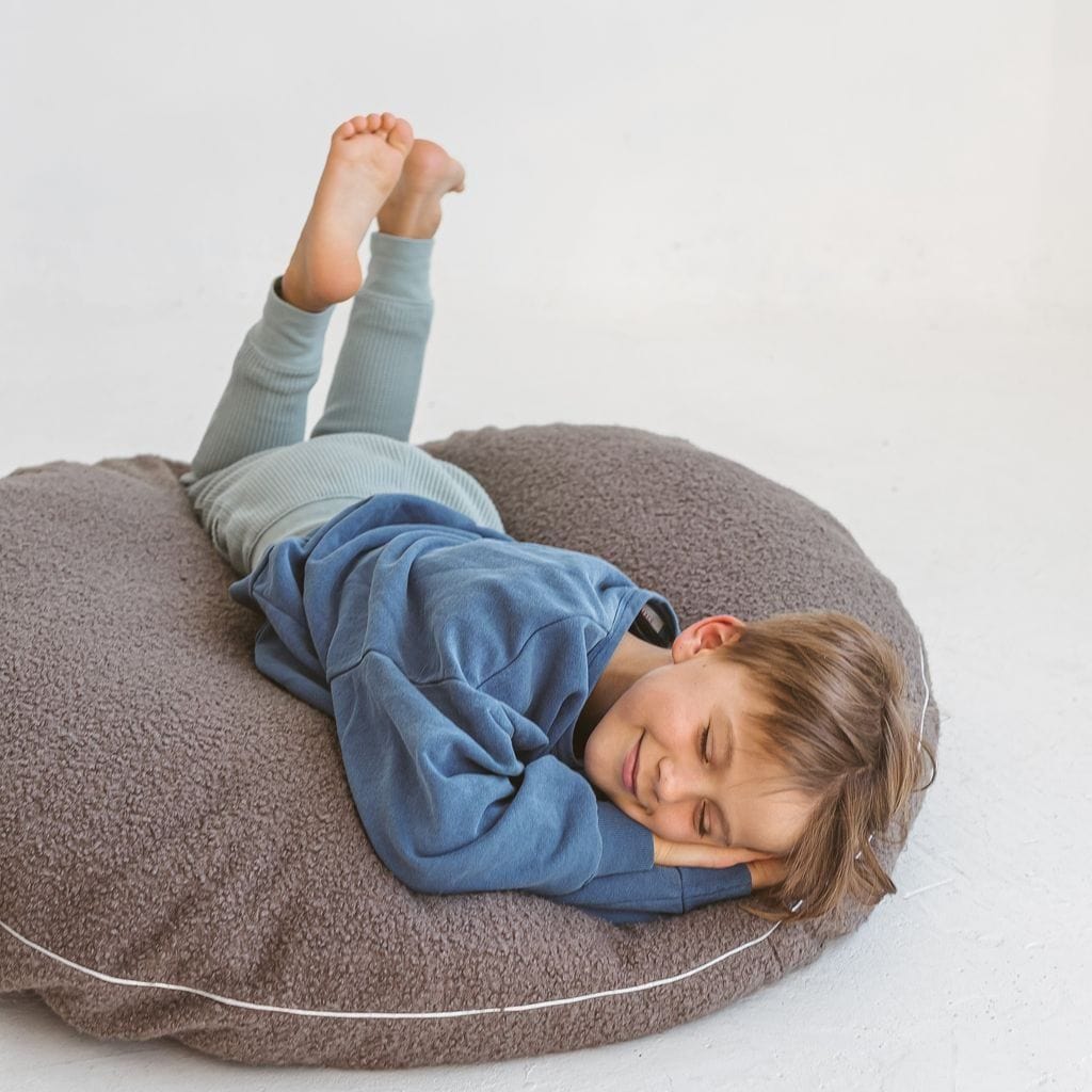 child lying on MINICAMP Boucle Fabric Kids Floor Cushion in Grey with feet in the air
