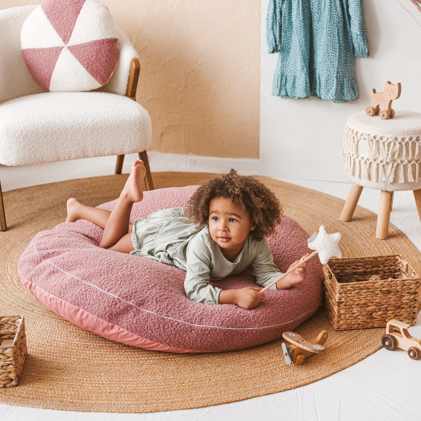 giel holding wand lying on MINICAMP Boucle Fabric Kids Floor Cushion in Rose in lounge
