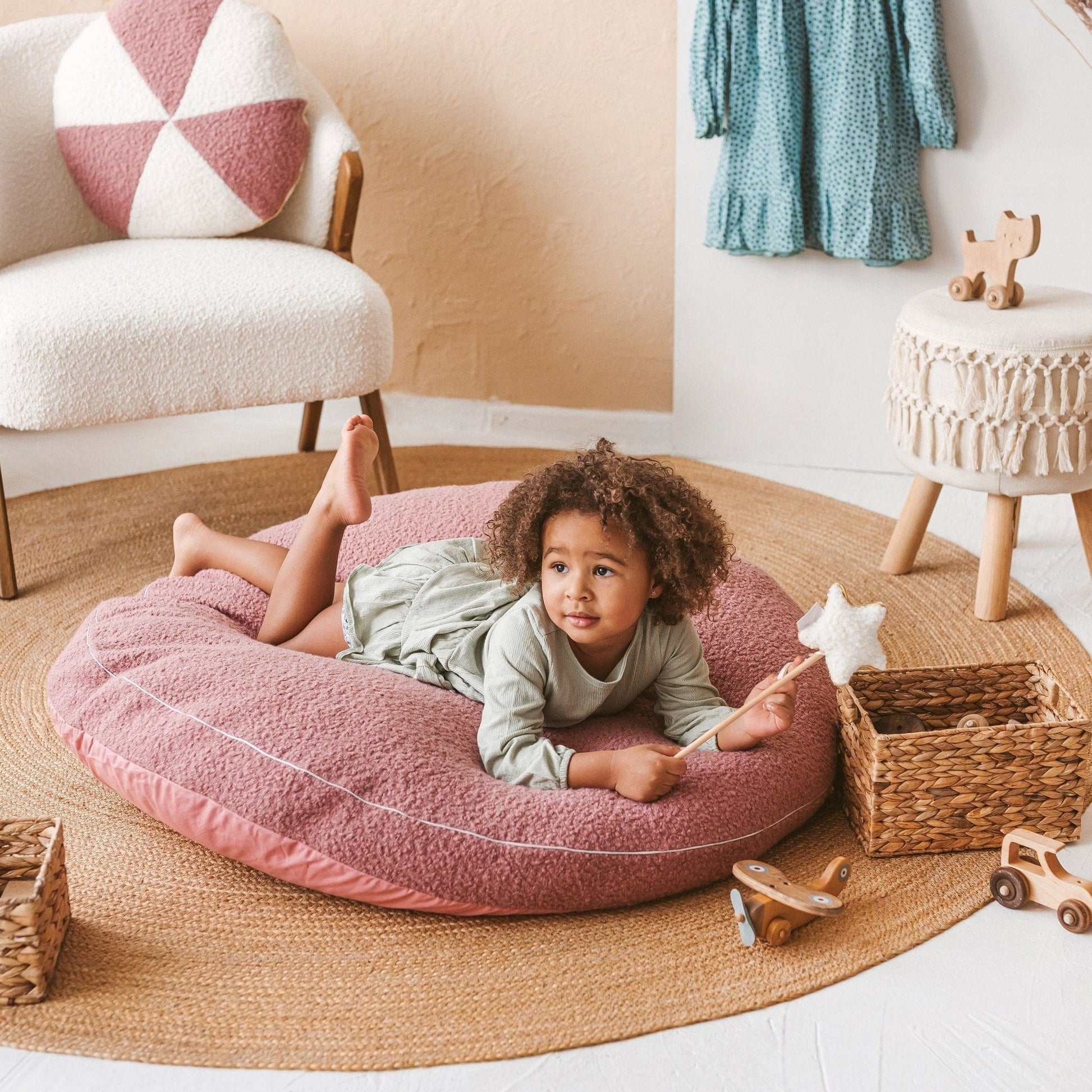 giel holding wand lying on MINICAMP Boucle Fabric Kids Floor Cushion in Rose in lounge
