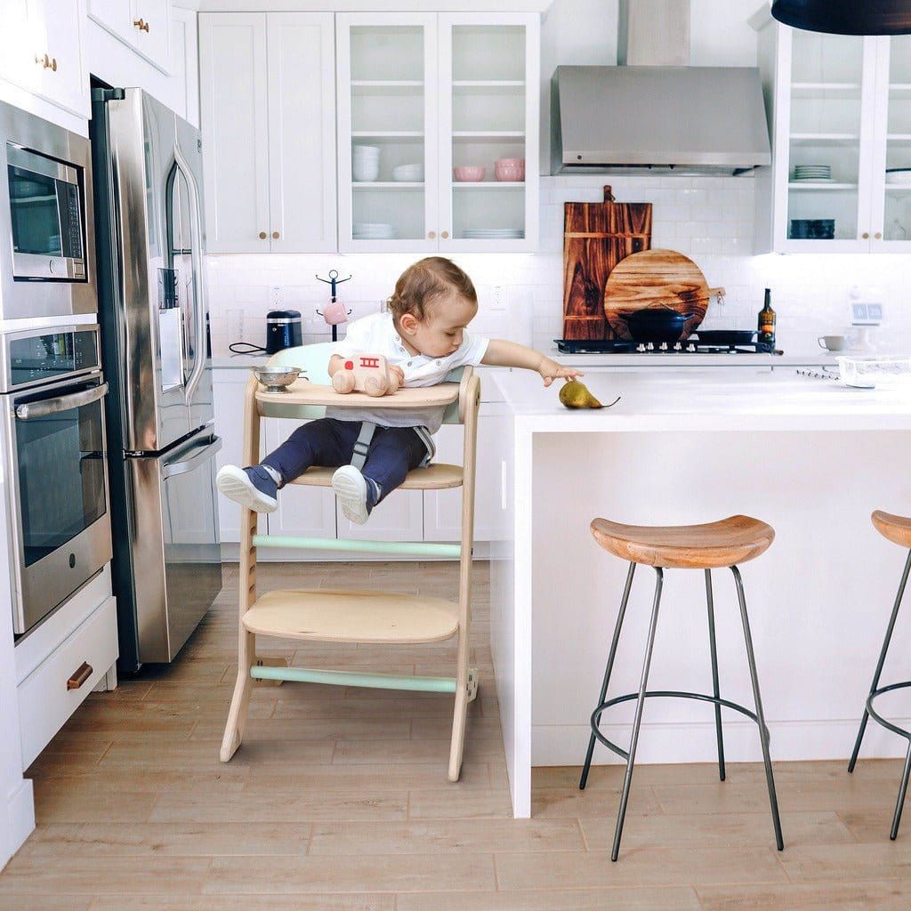 baby sitting in MamaToyz Mama High Chair in kitchen reaching for pear