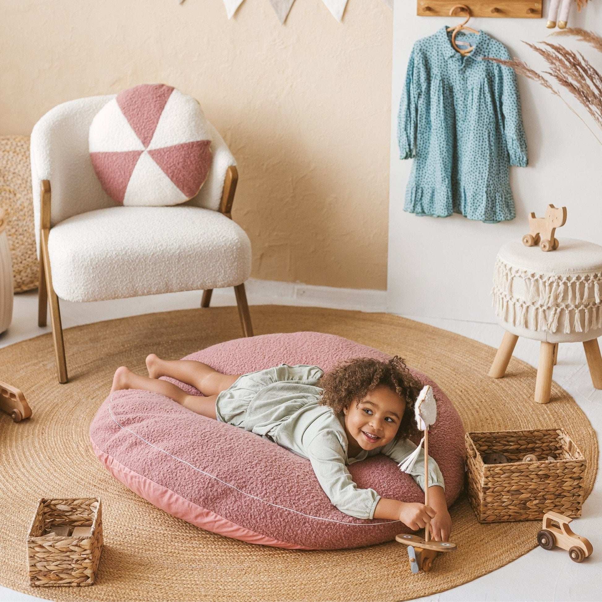 smiling girl lying on front on top of MINICAMP Boucle Fabric Kids Floor Cushion in Rose