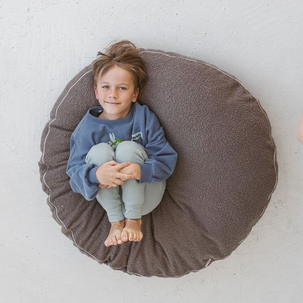 child holding knees to chest lying on MINICAMP Boucle Fabric Kids Floor Cushion in Grey