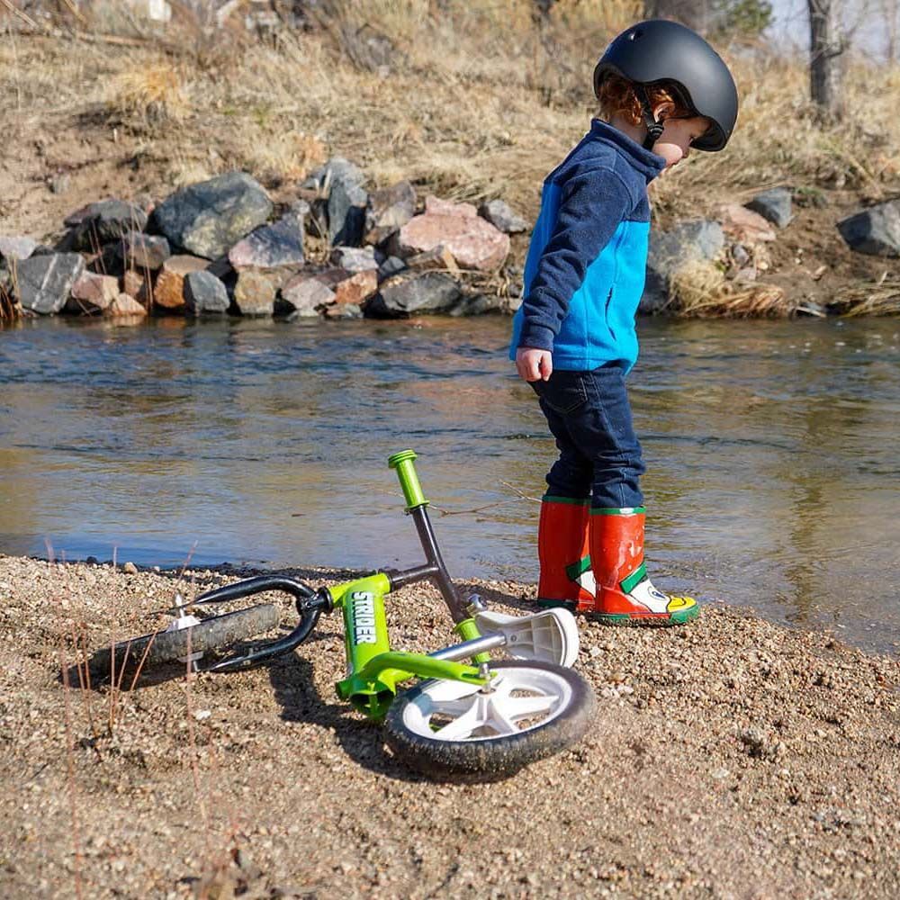 boy with Strider Classic 12 inch Balance Bike - Green next to stream