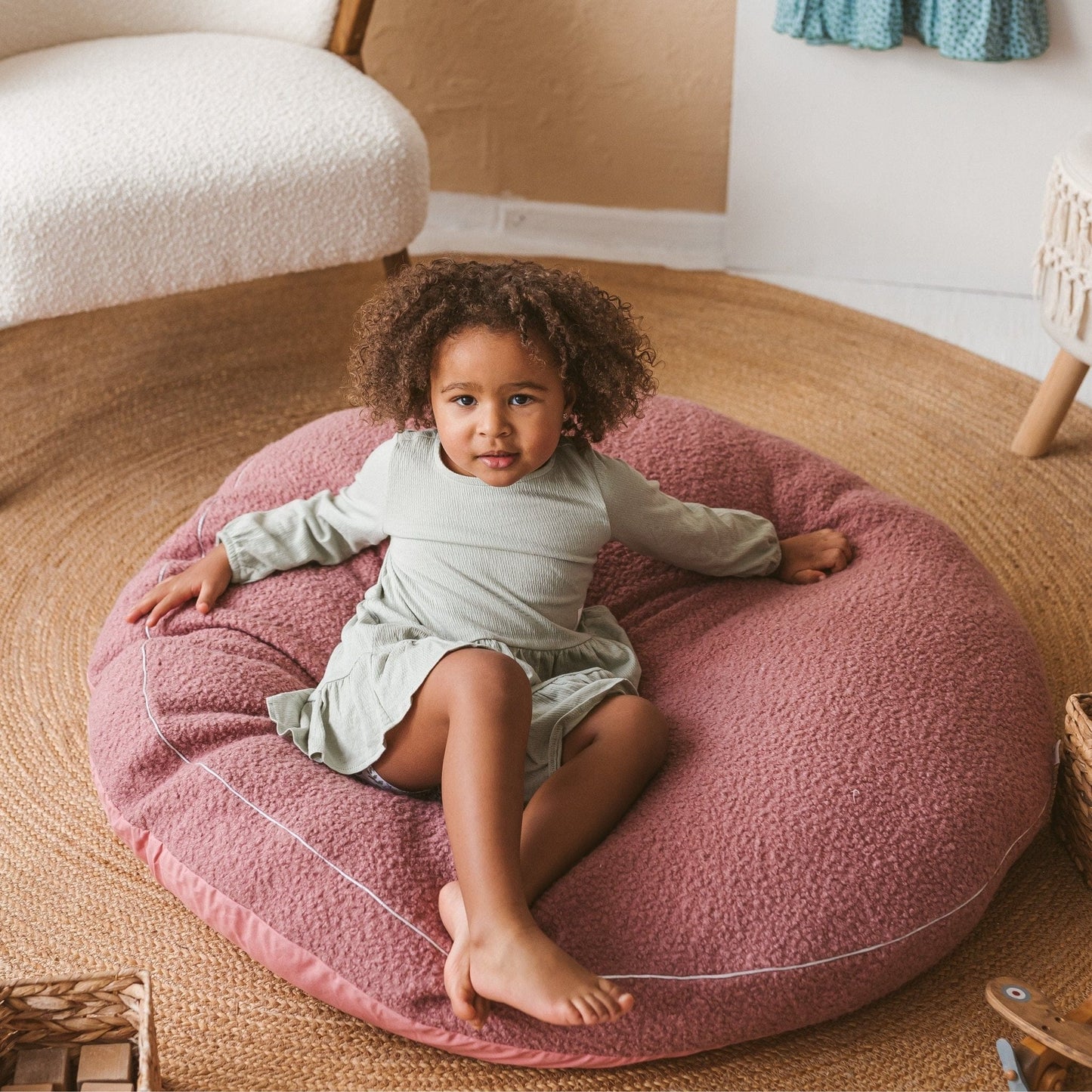 girl lying on back on MINICAMP Boucle Fabric Kids Floor Cushion in Rose