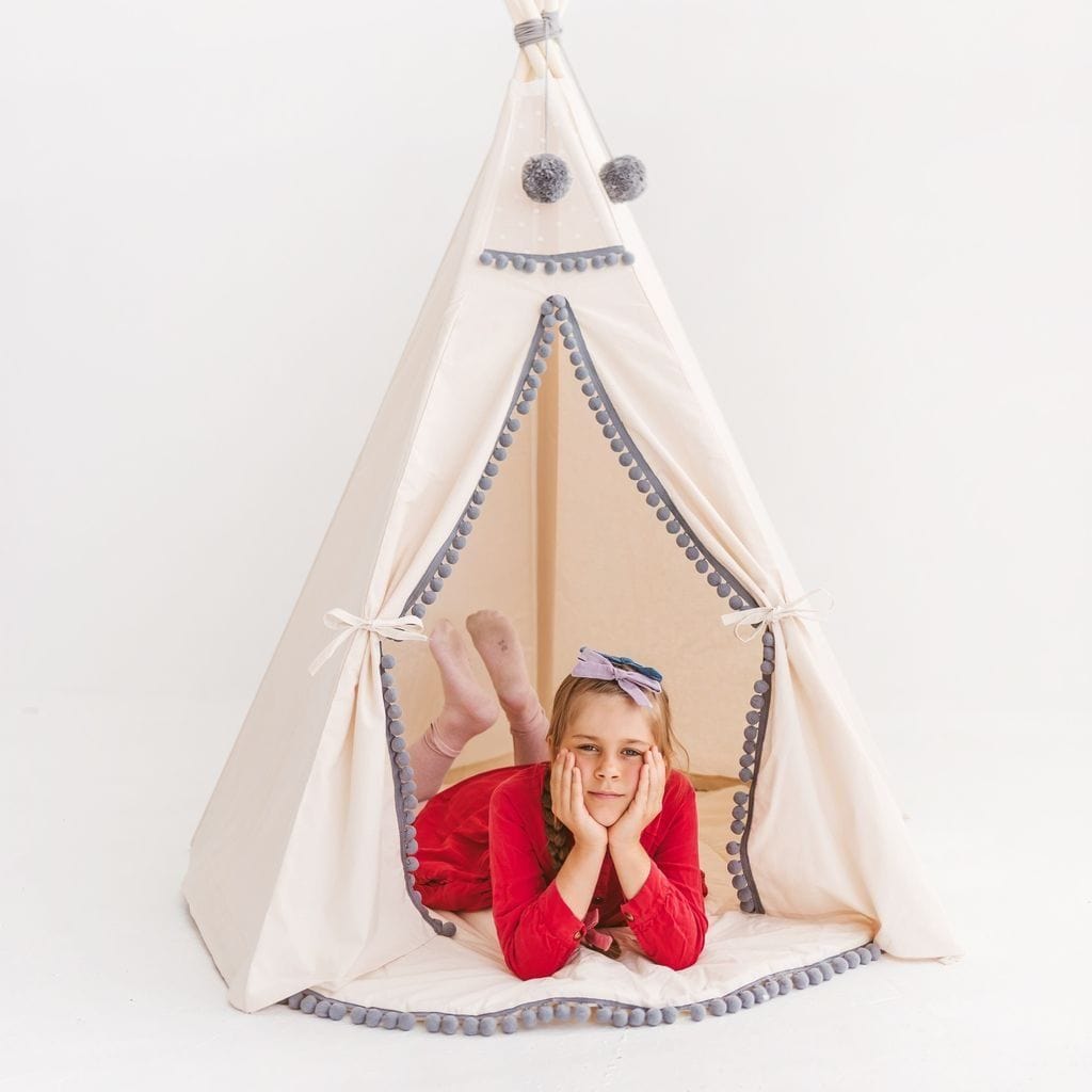 child lying in MINICAMP Kids Teepee in Off-White With Grey PomPoms