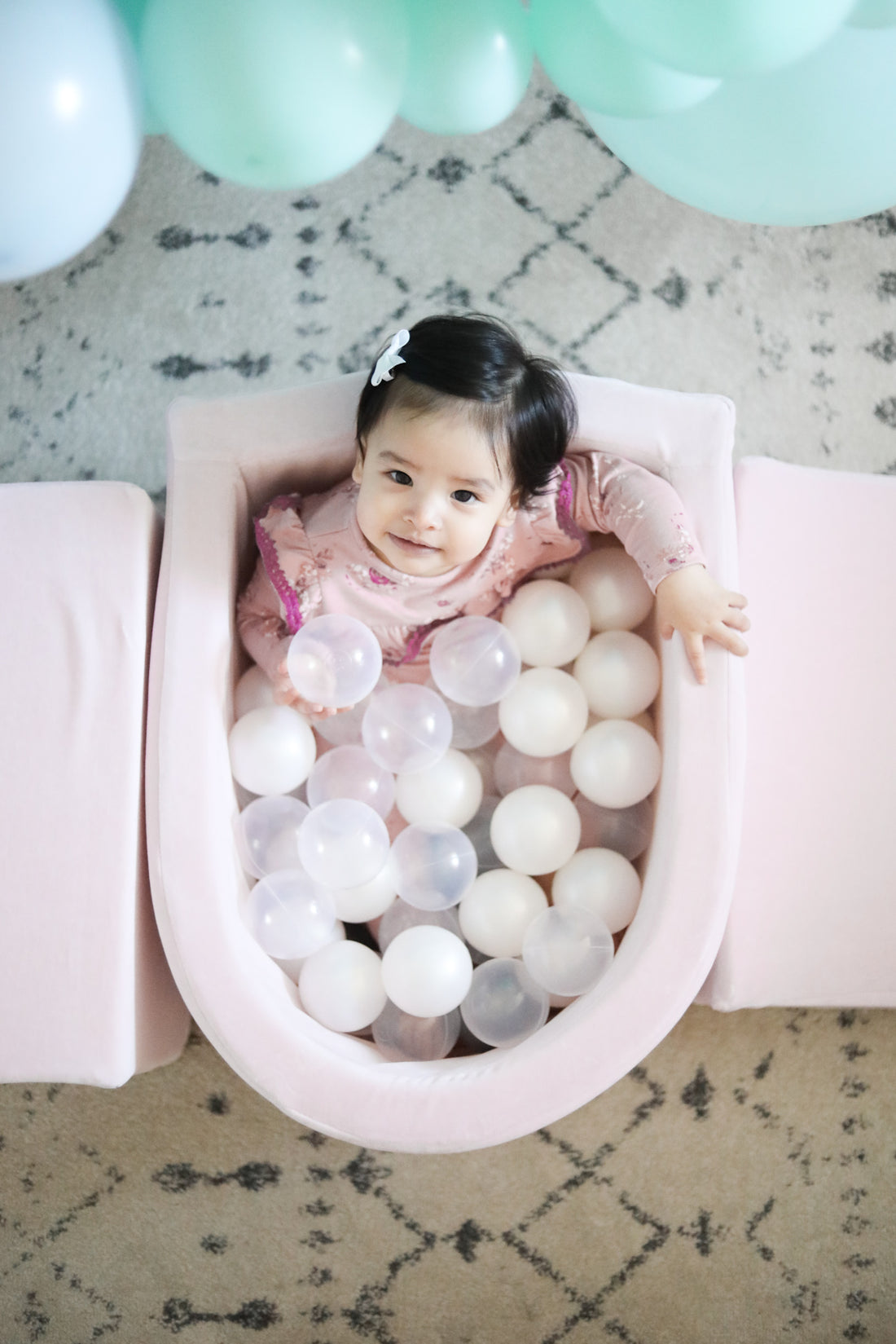 little girl sitting in meowbaby luxury ball pit and looking up