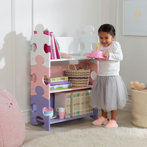 smiling girl holding cake in front of kidkraft puzzle bookshelf in pastel colours