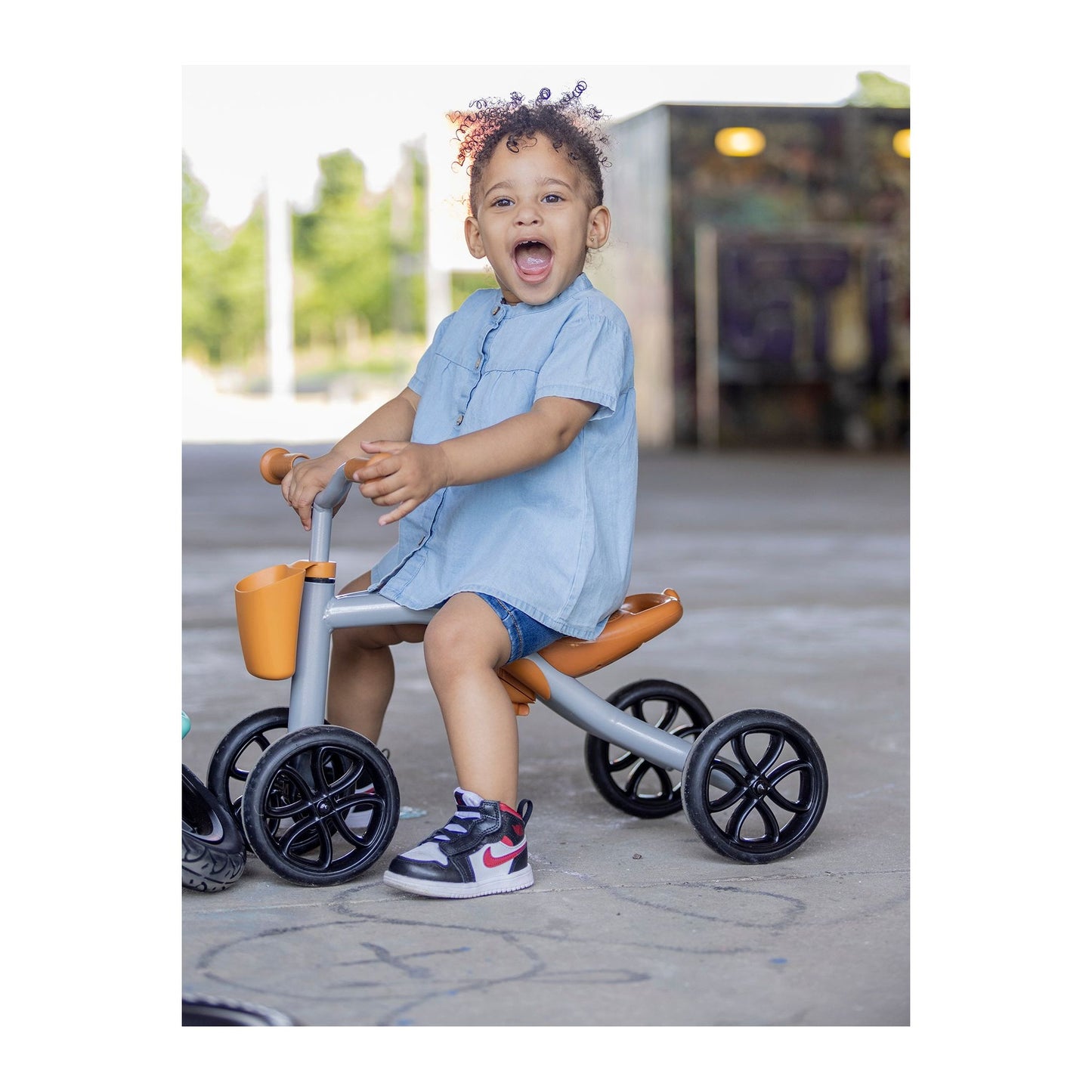 open mouthed child sitting on Chillafish Quadie 2 Ride-On and Basket Silver