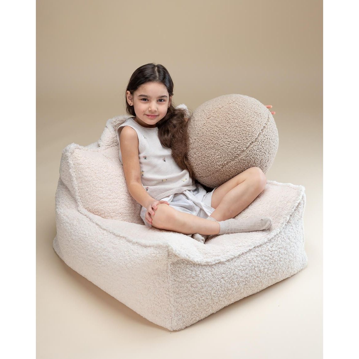 girl leaning back in beanbag chair holding Wigiwama Biscuit Ball Cushion