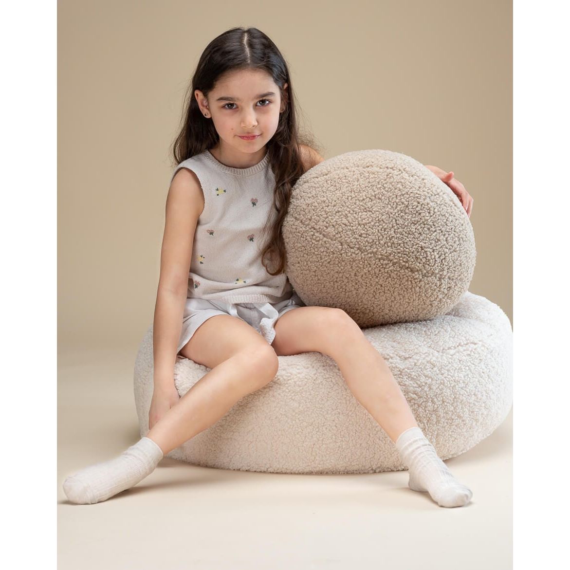 girl sitting on pouffe holding Wigiwama Biscuit Ball Cushion