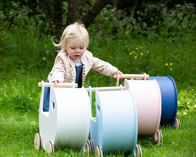 girl pushing moover wooden prams in white, blue and pink
