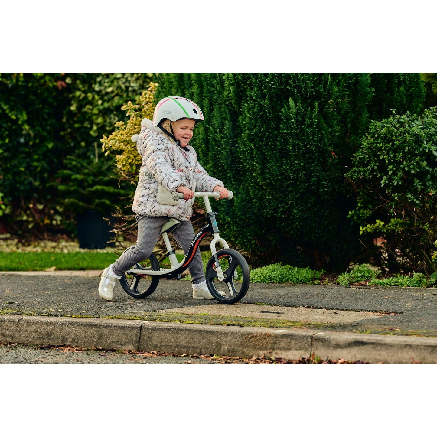 girl wearing Ride-Ezy Hector 54-57cms Kids Helmet - White and riding ride-ezy go glo balance bike on pavement