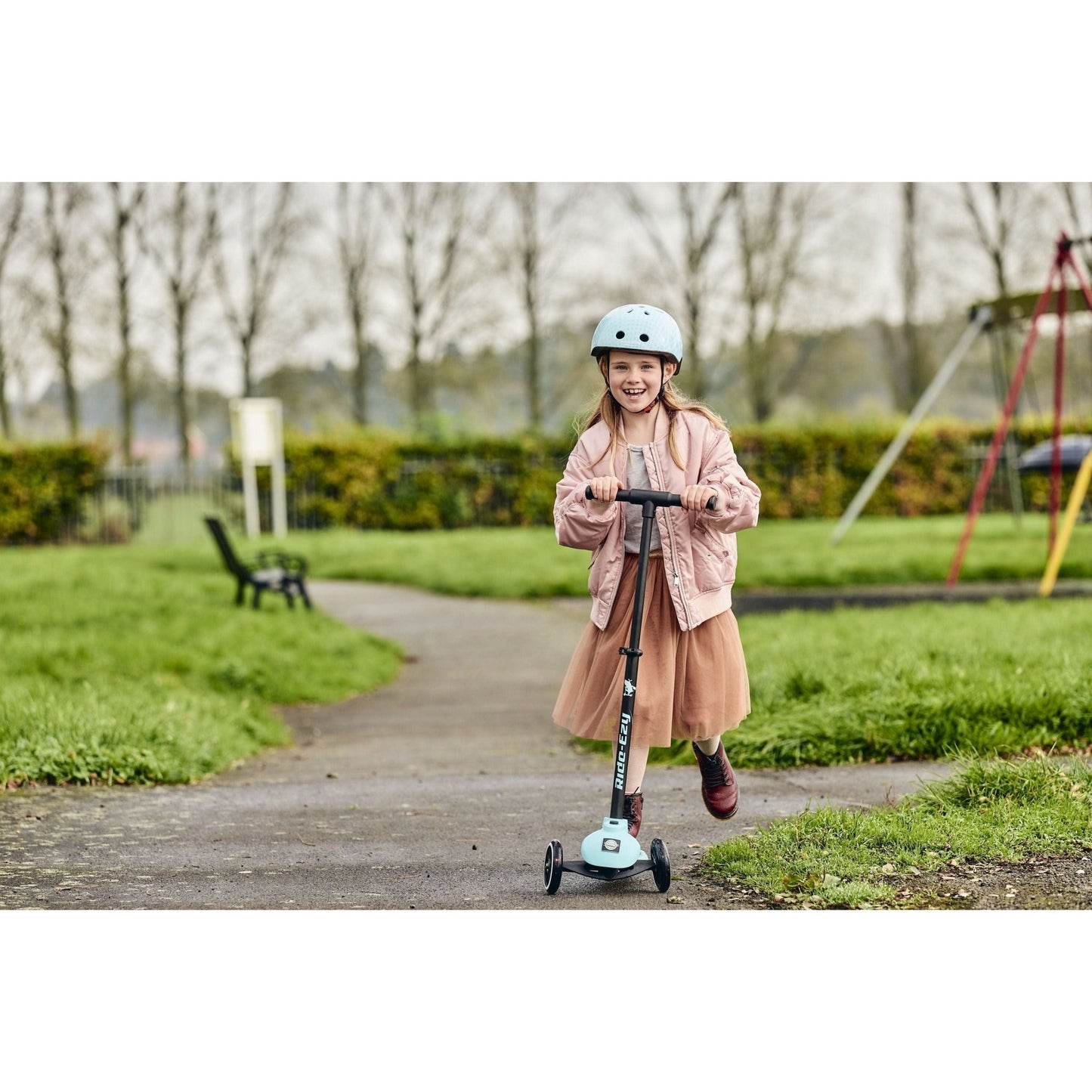 smiling girl riding Ride-Ezy Kick Scooter - Kingfisher in park near swings