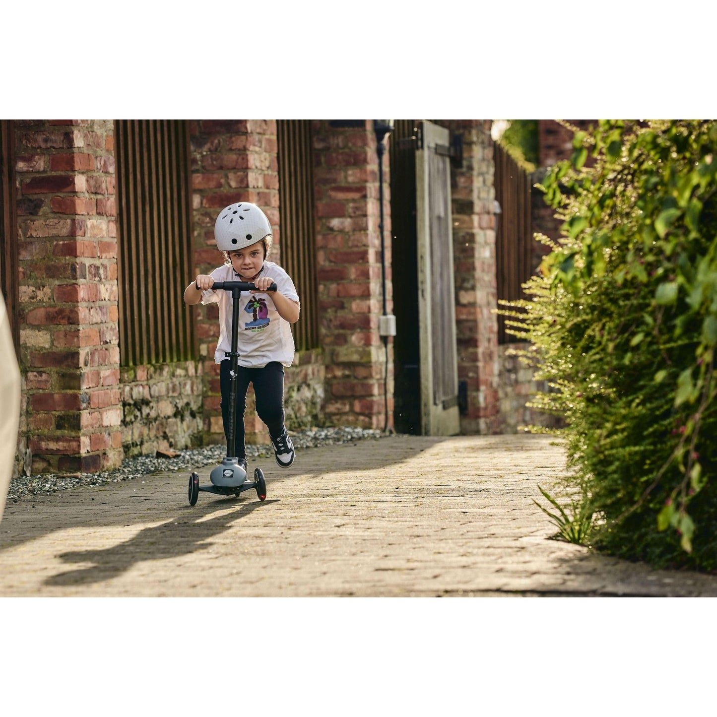 child riding Ride-Ezy Kick Scooter - Thunder Clouds on pathway near nedge