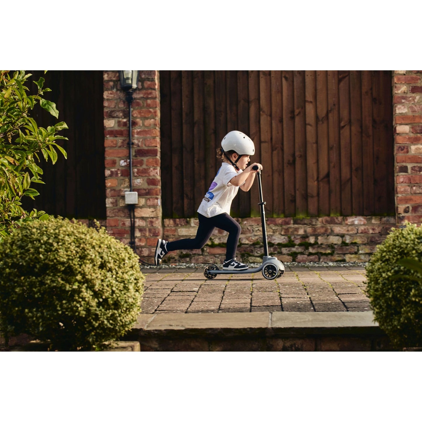 child riding Ride-Ezy Kick Scooter - Thunder Clouds on path in front of wooden fence