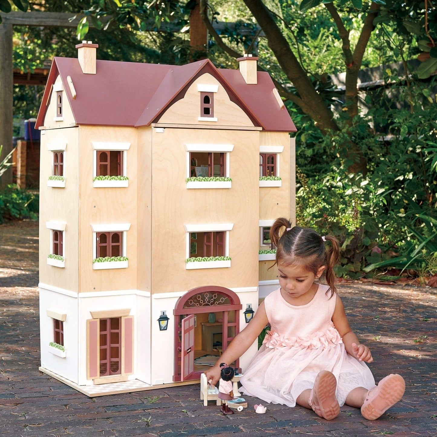 girl sitting in front of Tender Leaf Fantail Hall Deluxe Wooden Dolls House on patio