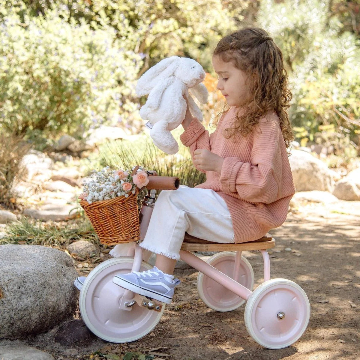 little girl holding teddy bear and riding banwood trike in pink