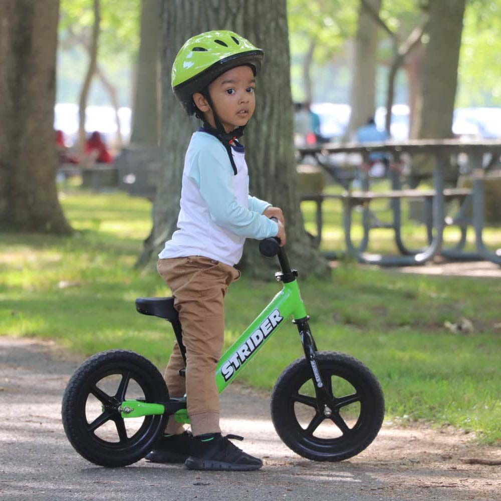 boy in helmet straddling Strider Sport 12 inch Balance Bike - Green