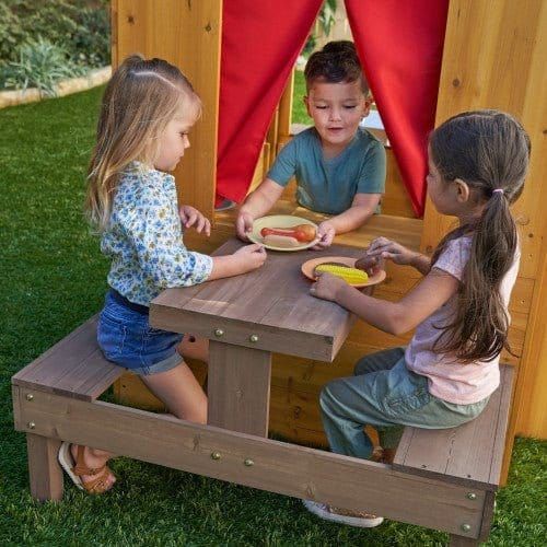 boy serving food to girls sitting at table of KidKraft Modern Outdoor Playhouse