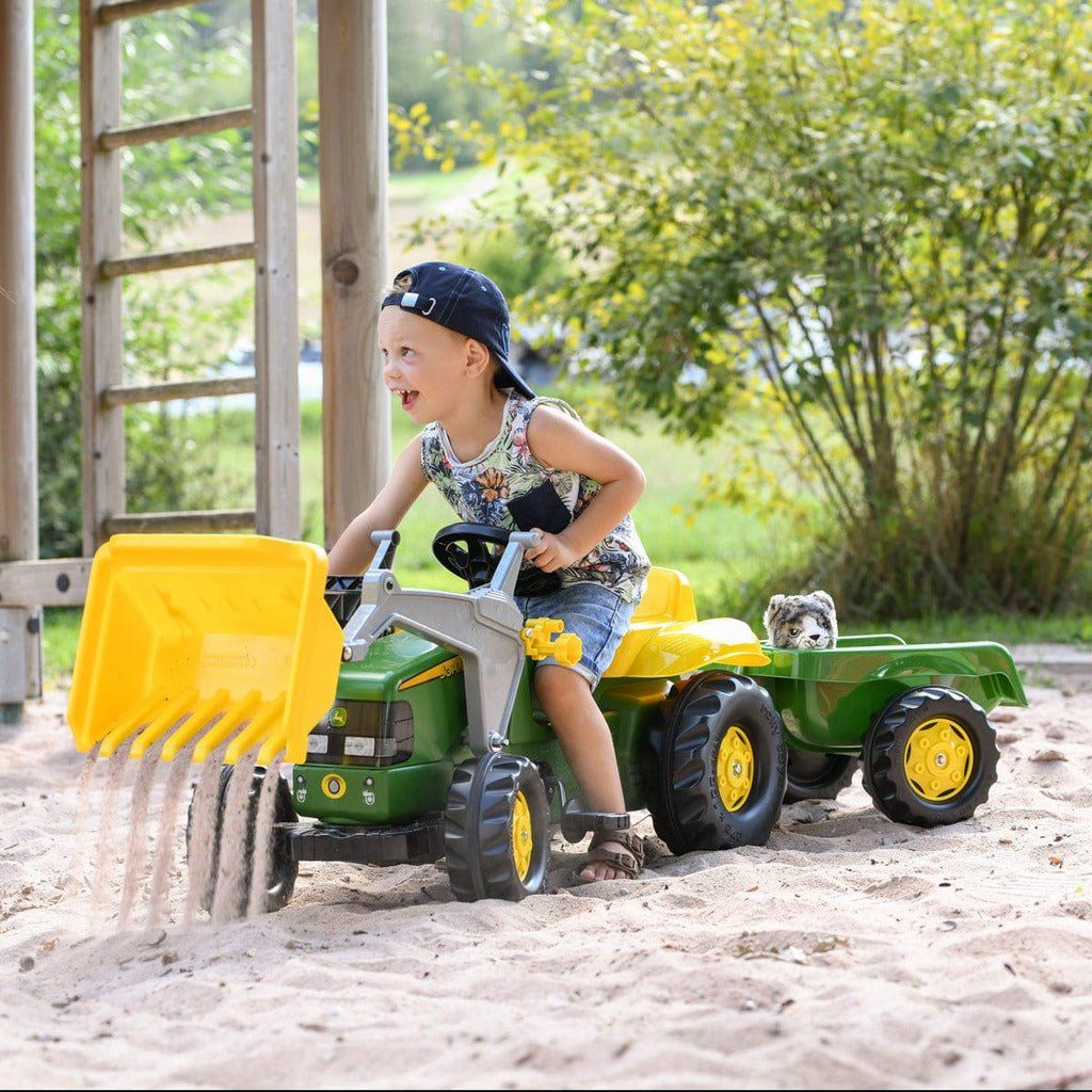 smiling boy riding Rolly Toys John Deere Tractor & Frontloader & Trailer in sandpit