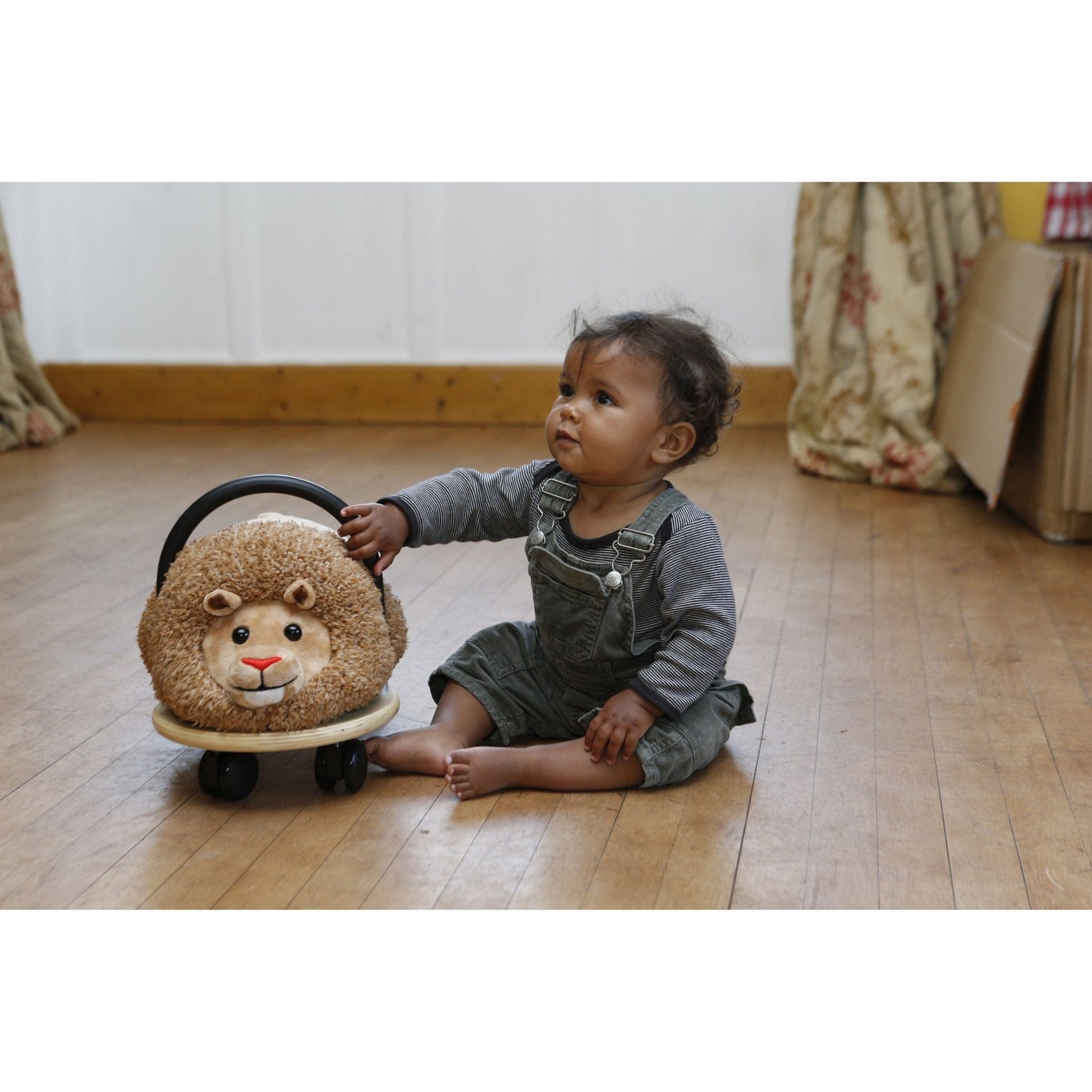 little girl sitting on floor with Wheelybug Plush Ride On - Lion front