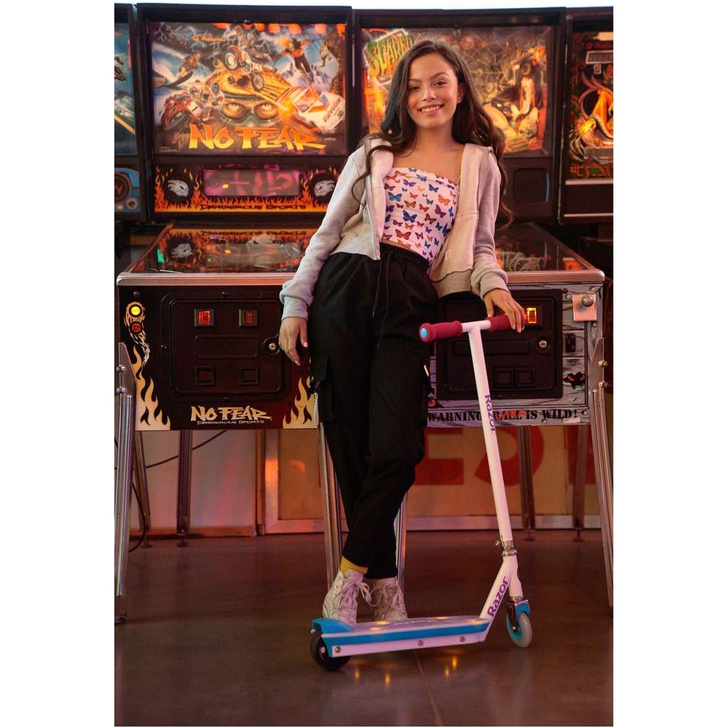 girl standing with Razor Electric Party Pop 10.8V Lithium-ion Scooter  in front of pinball machines