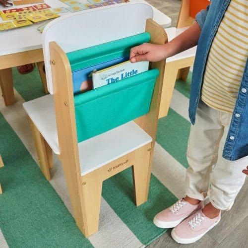 child getting book from storage pocket on chair of KidKraft Pocket Storage Table and 4 Chair Set - Natural