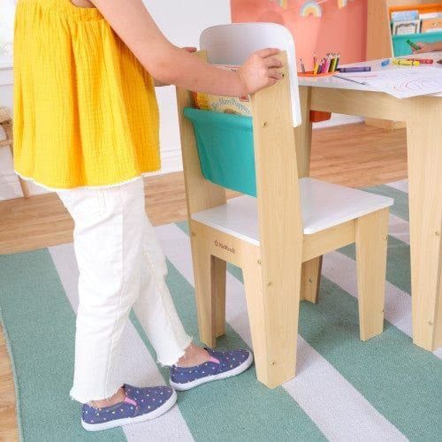 girl putting book in chair storage of KidKraft Pocket Storage Table & 2 Chair Set - Natural