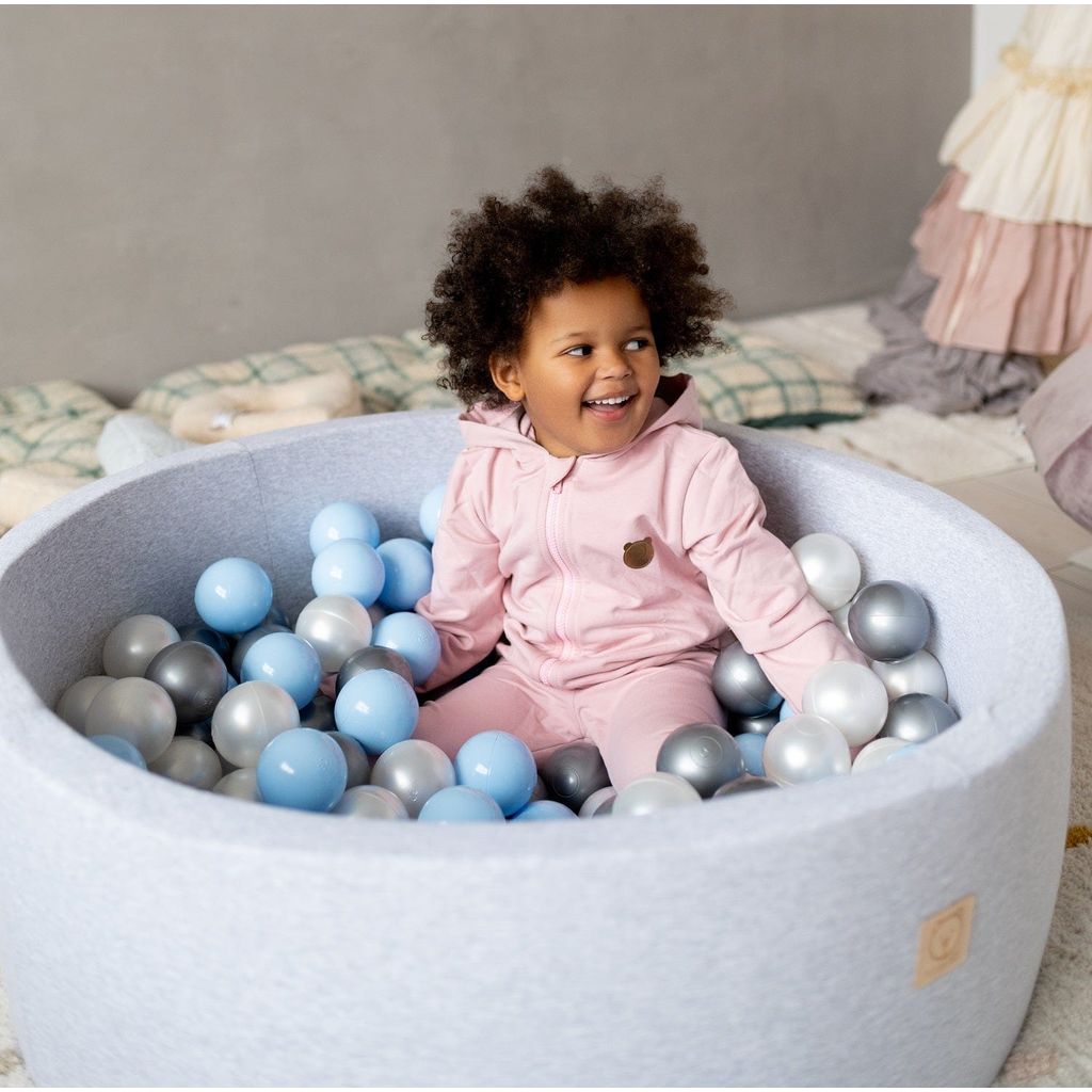 smiling child sitting in Misioo Joy Cotton Ball Pit Grey with 200 Grey and Blue Balls