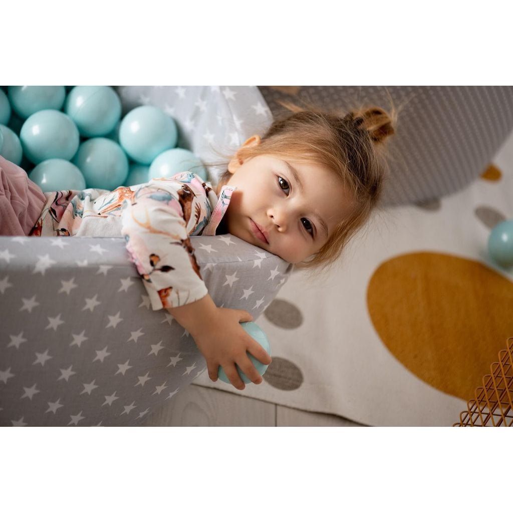 child lying in Misioo Cotton Ball Pit Grey and White Stars with 200 Blue & Grey Balls