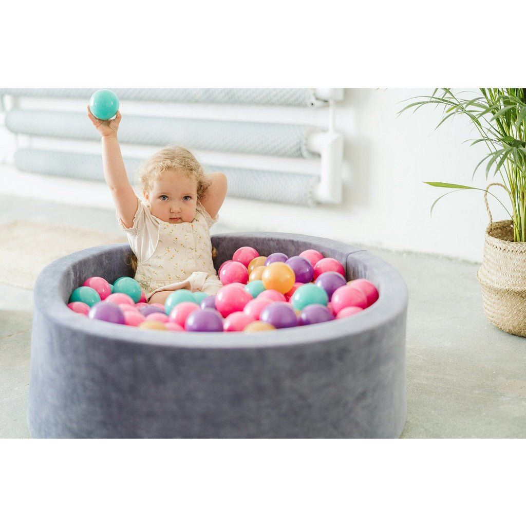 little girl holding green ball and issting in Velvet Round Foam Ball Pit with 200 Balls - Steel