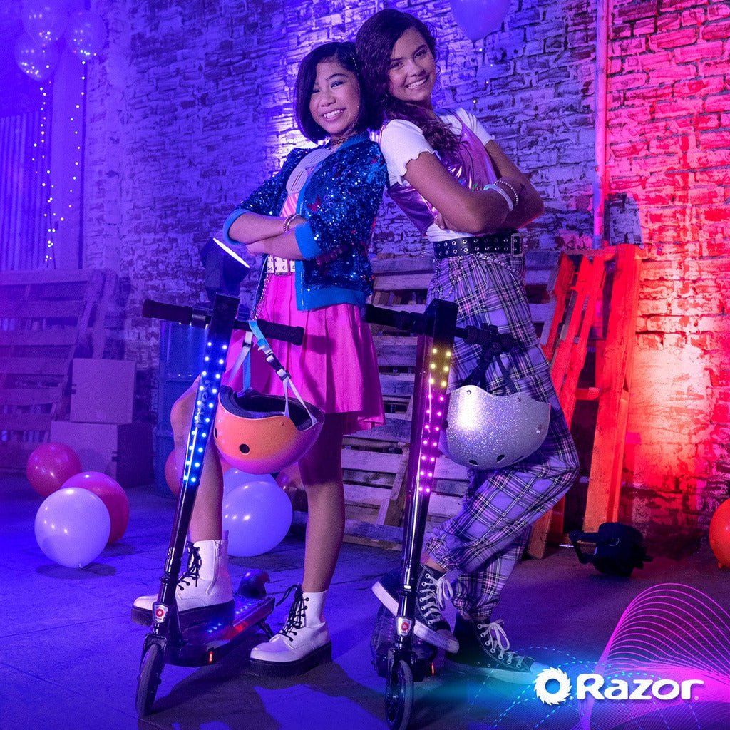 2 girls standing back to back with Razor Sonic Glow Bluetooth 24 Volt Scooters
