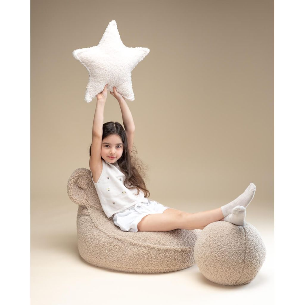 girl sitting on bear lounger holding Wigiwama Cream White Star Cushion in the air