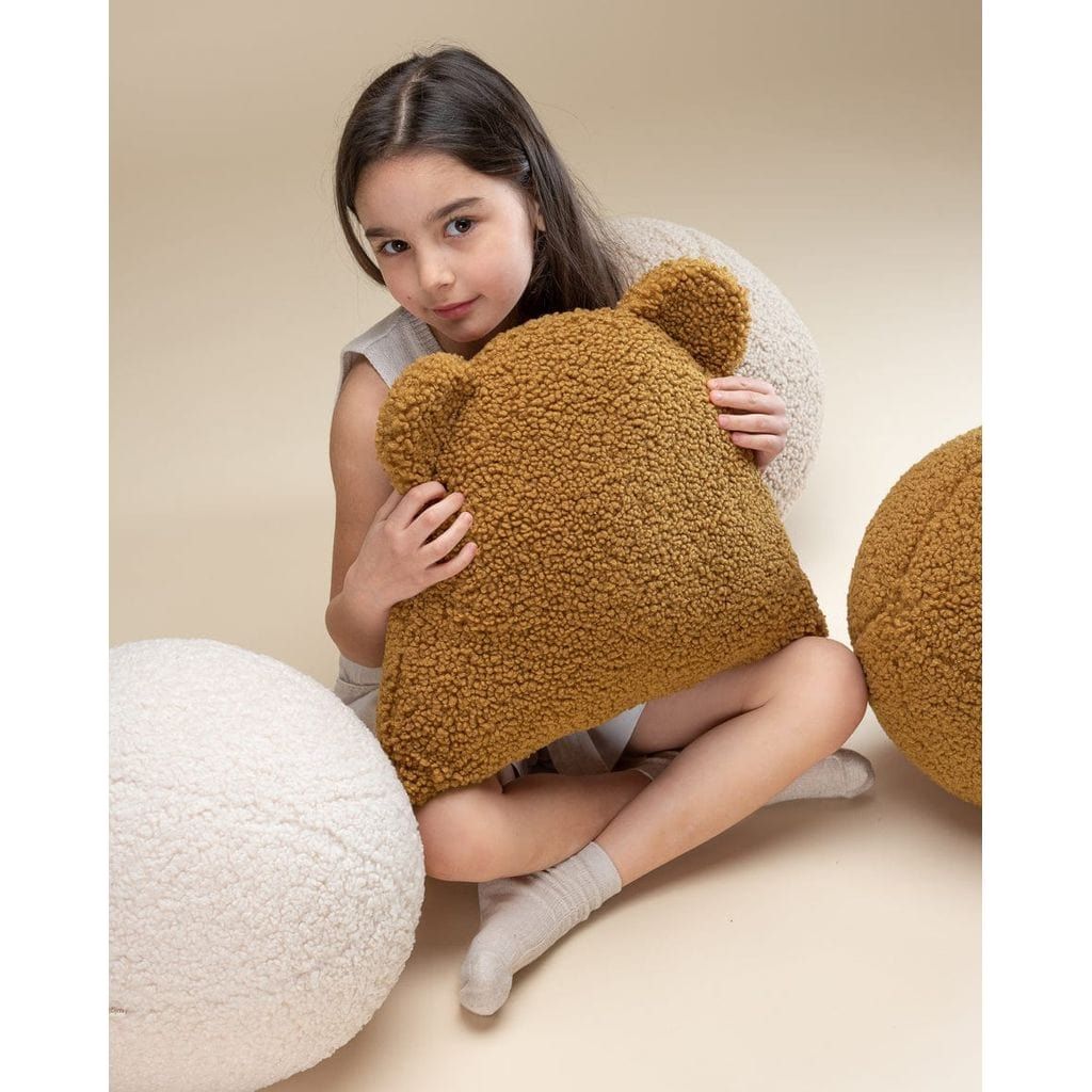 girl sitting holding Wigiwama Cream White Ball Cushion and teddy bear cushion