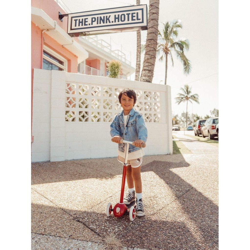 Boy riding Banwood Scooter Age 3+ in Red in front of The Pink Hotel