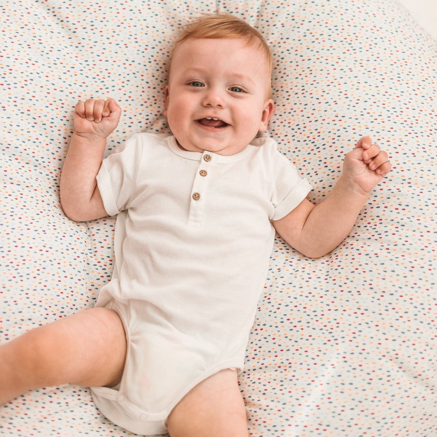 close up of smiling baby lying on MINICAMP Big Floor Cushion With Pompoms in Colour Drops on White