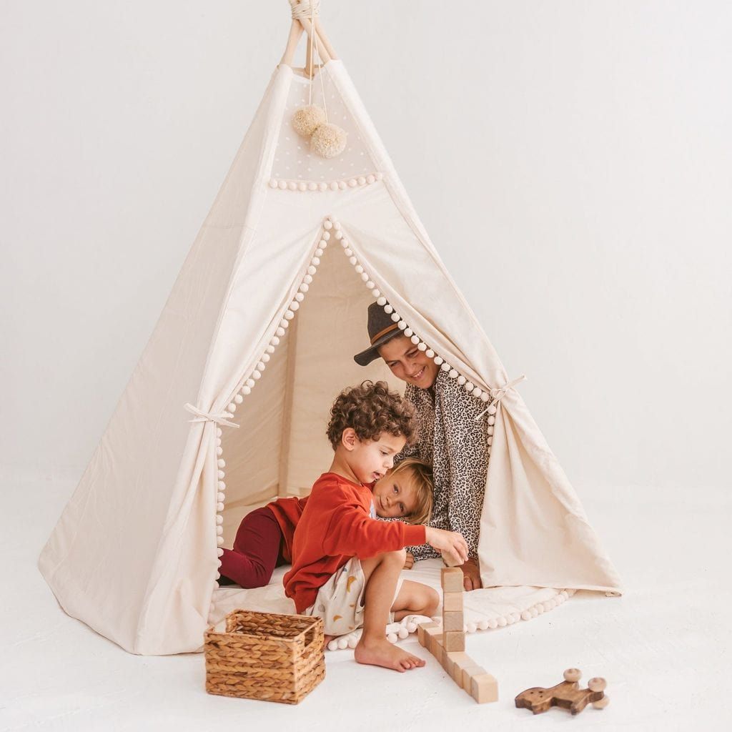 three children playing in MINICAMP Extra Large Kids Teepee Tent With Pom Pom Decor