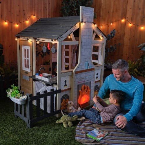 man and boy sitting on rug by KidKraft Cozy Hearth Cabin Playhouse at night 