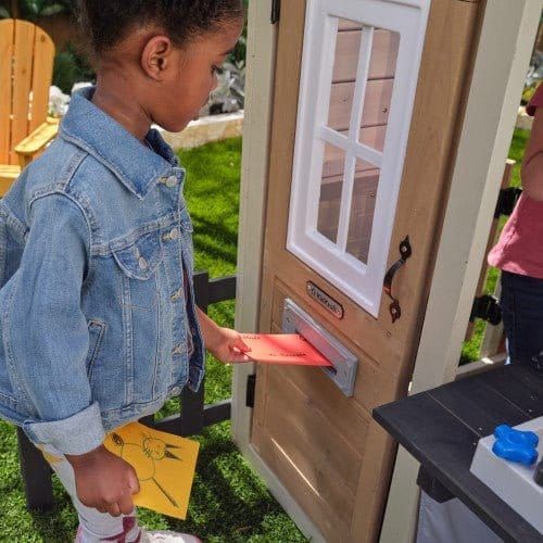 girl posting letters through door of KidKraft Cozy Hearth Cabin Playhouse