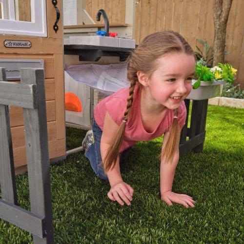 girl on hands and knees in KidKraft Cozy Hearth Cabin Playhouse